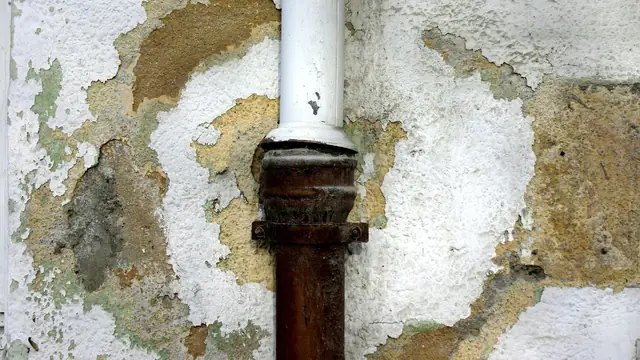 Peeling paint and stained plaster around a pipe on a wall
